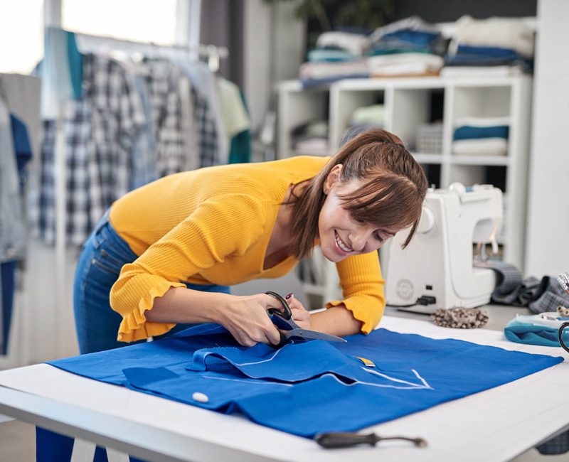 Dedicated seamstress standing next to table and cutting textiles for elegant dress.